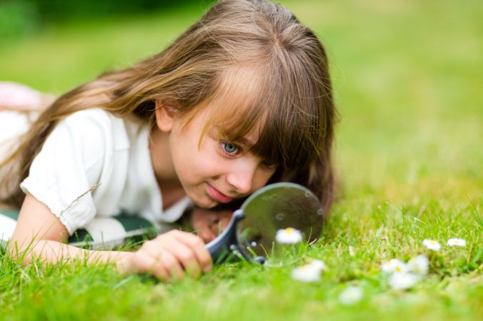 Girl with magnifying glass taking a close look at a flower.